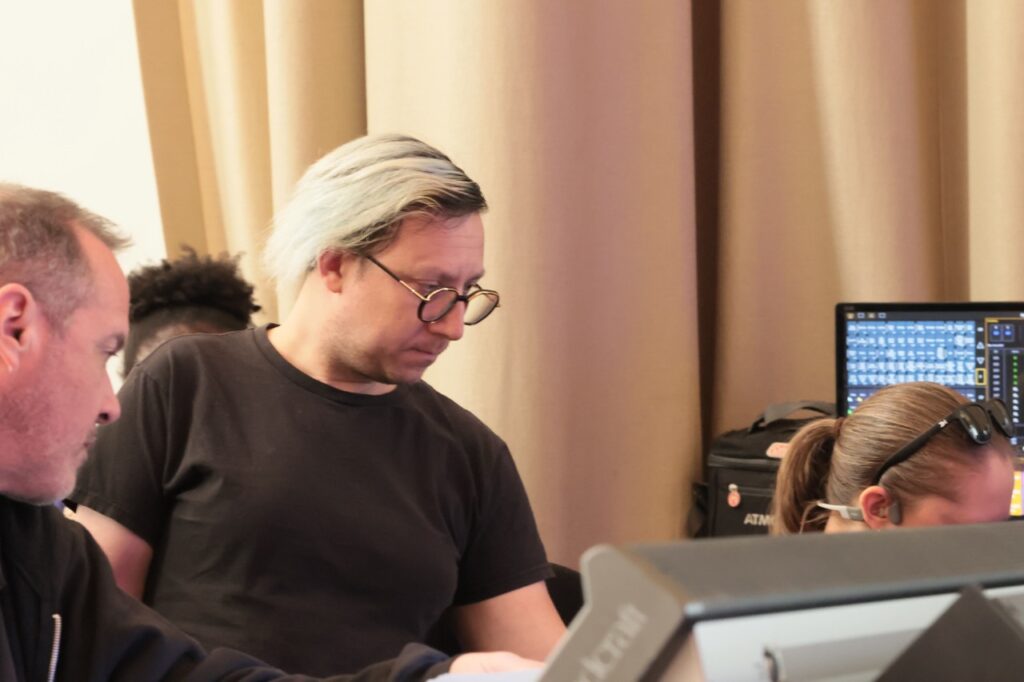 A white gentleman with blonde hair and circle glasses looks on as a woman works on a computer.