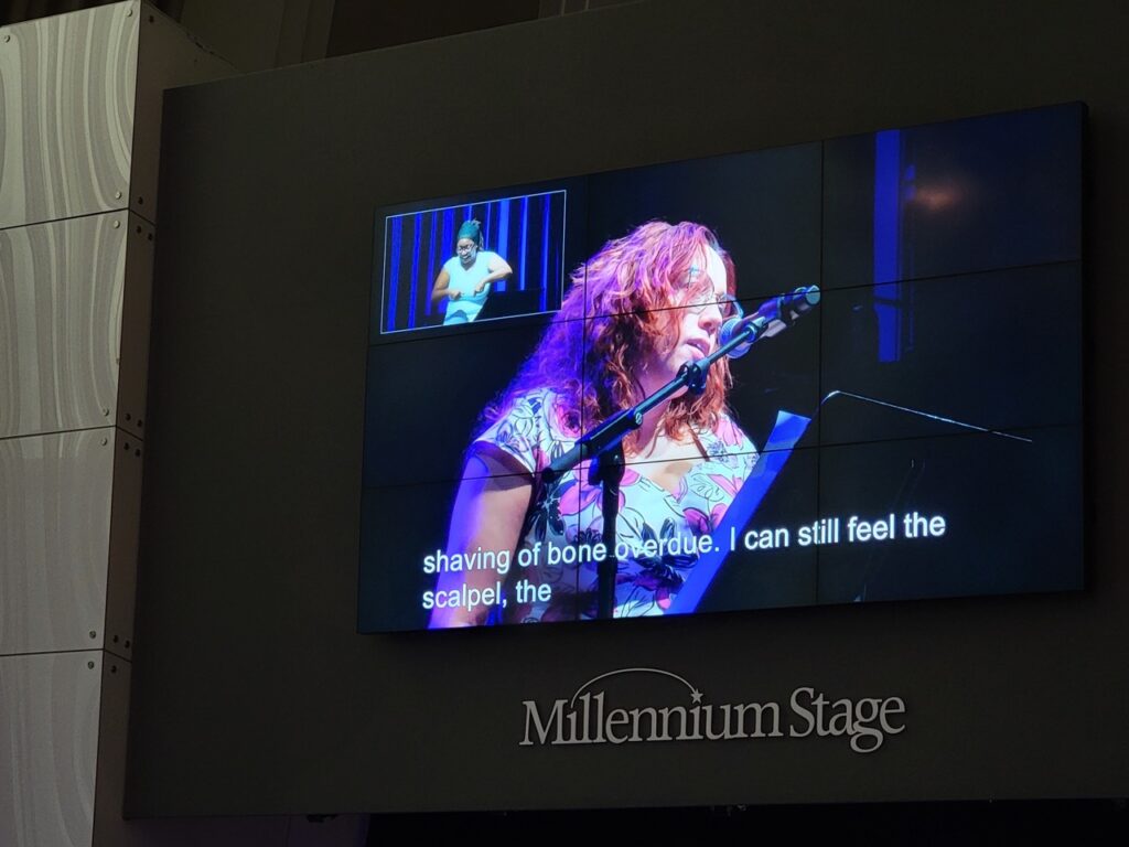 A large screen shows a woman with wavy brown hair singing and a picture in picture has an African American woman signing.